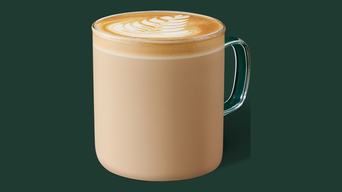 Officiële Starbucks-productfoto van een Flat White met latte art in een glazen mok op een groene achtergrond